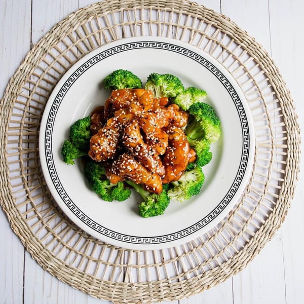 Howard Wang's Preston Hollow's sesame chicken with broccoli on a white plate with a patterned rim.