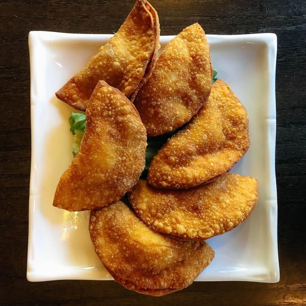 Six golden-brown fried dumplings, likely potstickers or wontons, arranged on a white rectangular plate.