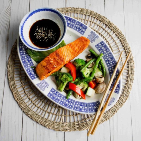 Asian salmon dish with stir-fried vegetables and a side of soy sauce with sesame seeds.
